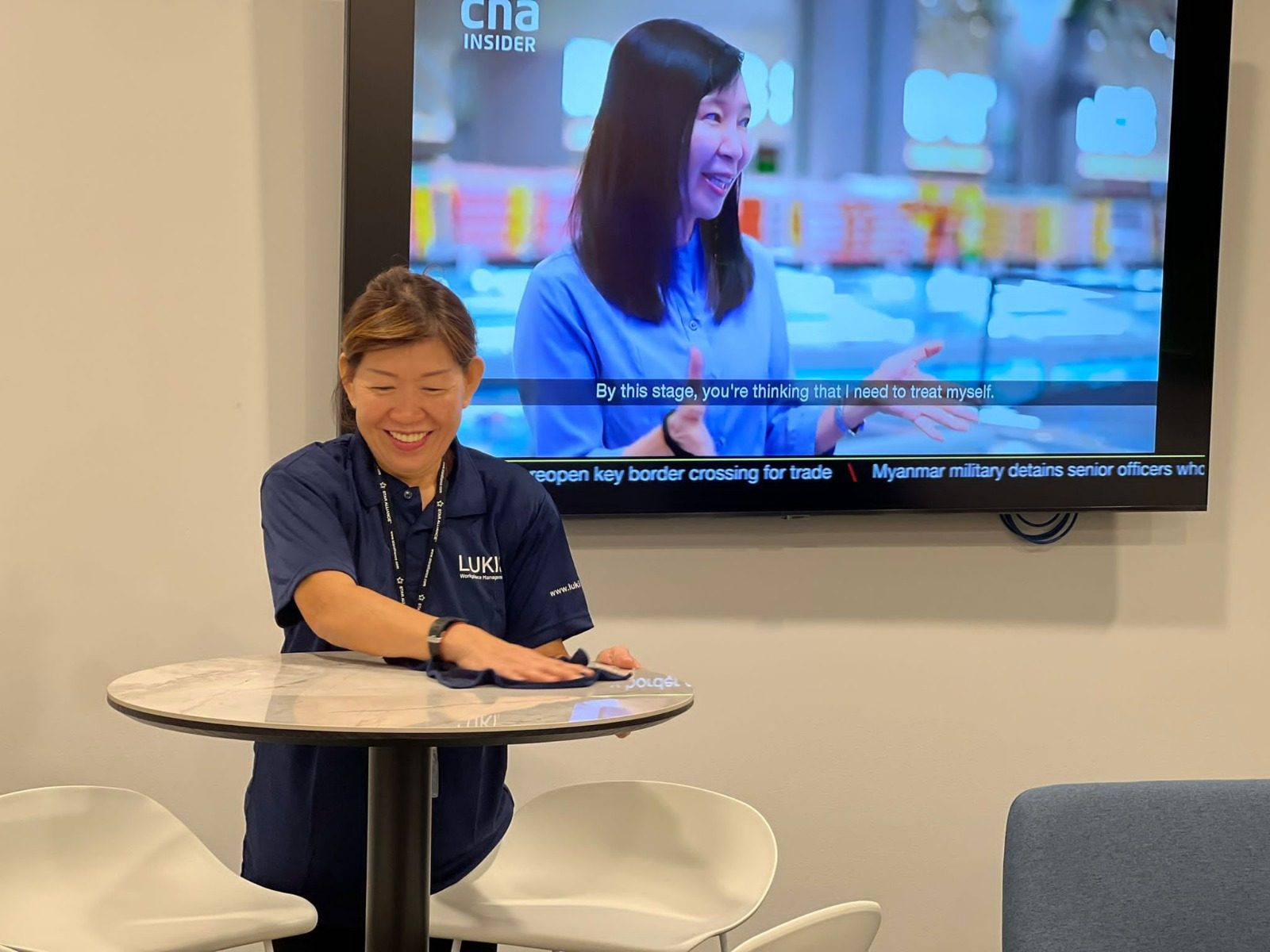 Smiling Lukis office cleaner wiping down a meeting room table in a Singapore office